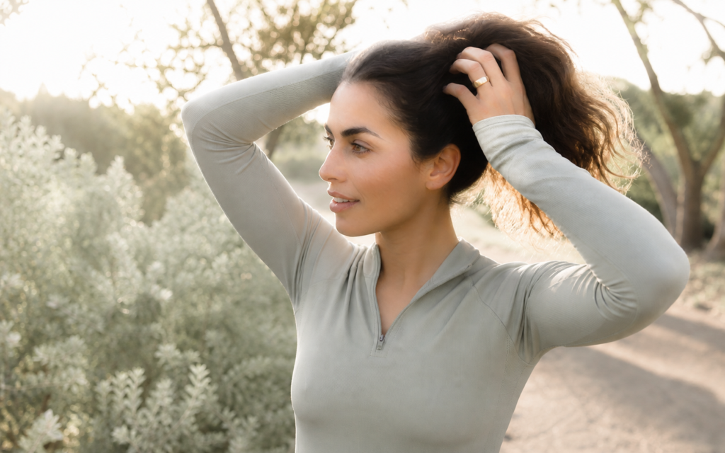 Woman wearing a gold Oura Ring outdoors while adjusting her hair in warm evening sunlight